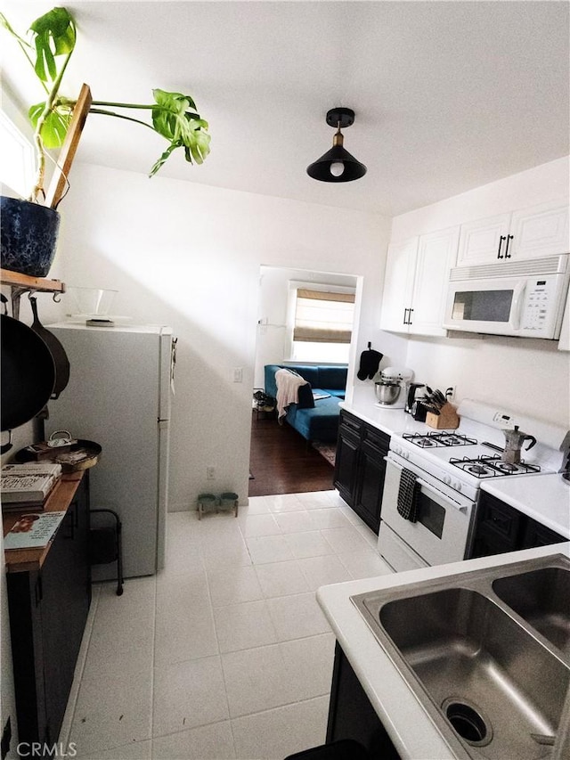kitchen featuring light tile patterned floors, dark cabinetry, white appliances, white cabinetry, and a sink