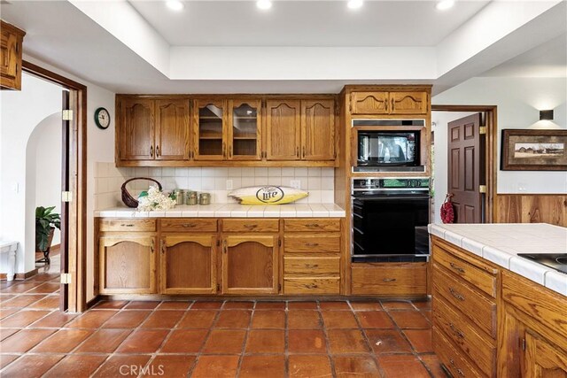 13155 San Antonio Rd, Atascadero, CA 93422 - kitchen featuring tasteful backsplash, brown cabinetry, tile countertops, arched walkways, and black appliances
