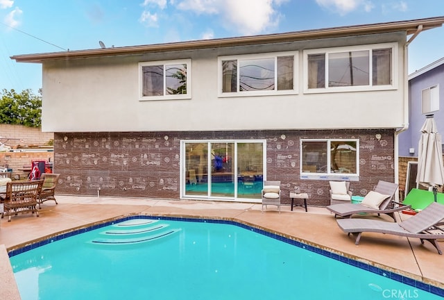 rear view of house with a patio area, stucco siding, an outdoor pool, and brick siding
