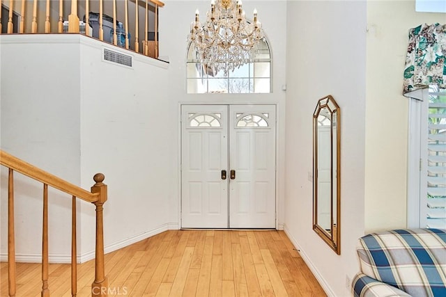 entryway with visible vents, hardwood / wood-style flooring, a high ceiling, an inviting chandelier, and stairs
