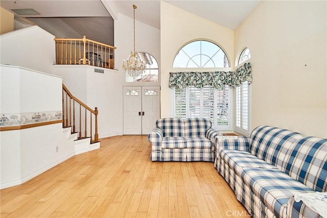 living room with baseboards, stairs, an inviting chandelier, wood finished floors, and high vaulted ceiling