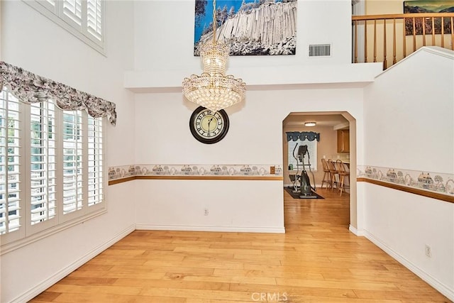 unfurnished room with visible vents, a high ceiling, an inviting chandelier, and wood finished floors