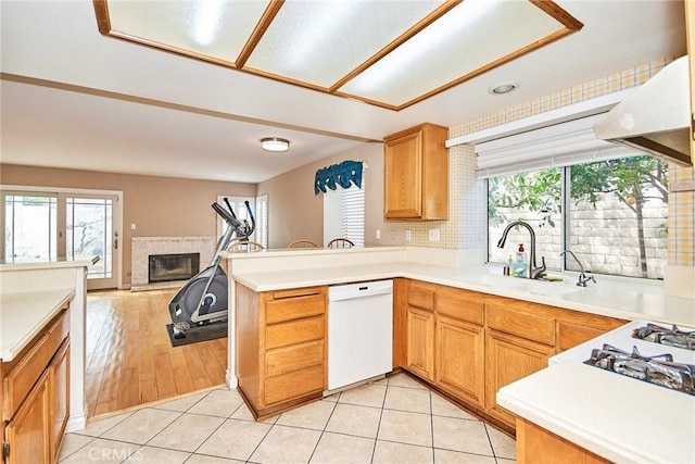 kitchen with a sink, a glass covered fireplace, white dishwasher, and light tile patterned floors
