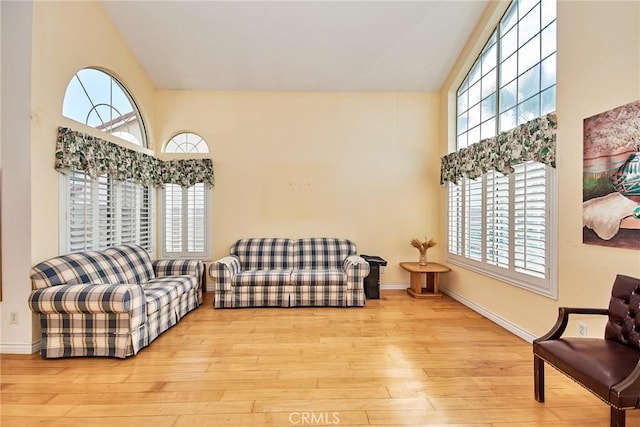 living area with high vaulted ceiling, baseboards, and wood finished floors