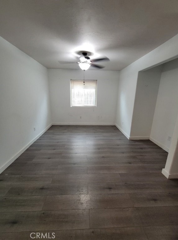 unfurnished room with baseboards, dark wood-style flooring, and ceiling fan