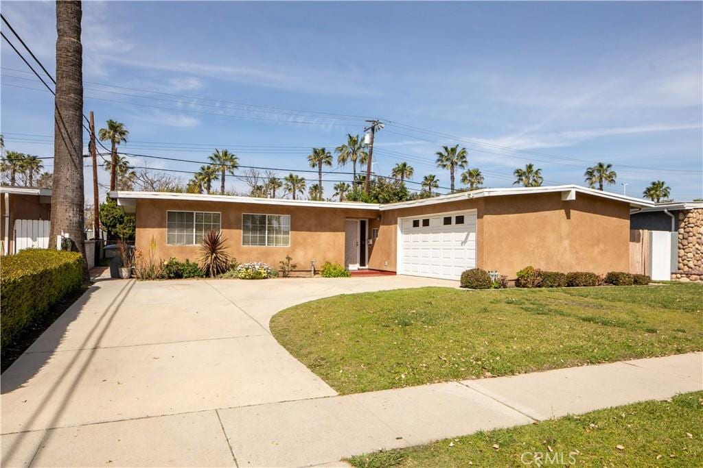 ranch-style home featuring concrete driveway, a garage, a front yard, and stucco siding