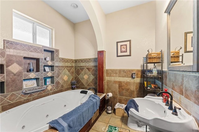 bathroom with a wainscoted wall, a whirlpool tub, a sink, tile patterned flooring, and tile walls