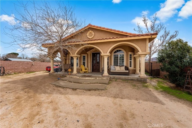 mediterranean / spanish-style home with a tiled roof, fence, covered porch, and stucco siding