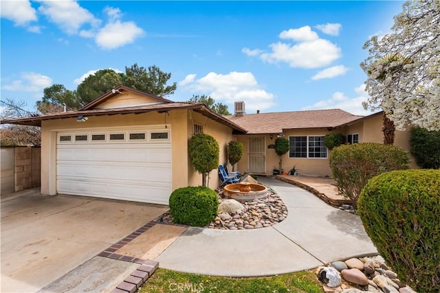 ranch-style home with an outdoor fire pit, stucco siding, an attached garage, and concrete driveway