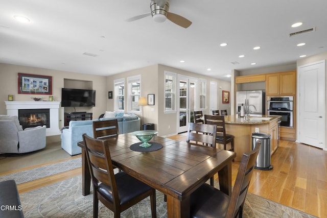 dining area featuring light wood finished floors, visible vents, a ceiling fan, and a glass covered fireplace