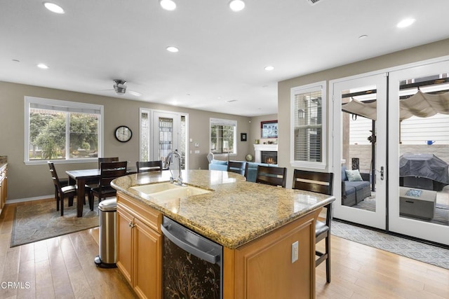 kitchen featuring a ceiling fan, a warm lit fireplace, a sink, light wood-style floors, and dishwasher