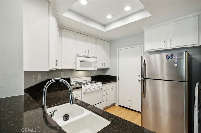kitchen with white cabinets, recessed lighting, a raised ceiling, a sink, and white appliances