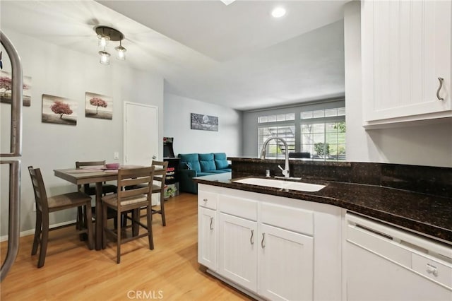 kitchen with dark stone counters, a sink, dishwasher, light wood-style flooring, and white cabinets