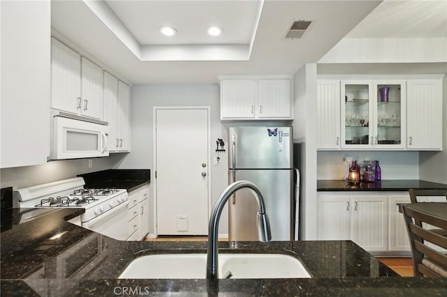 kitchen with dark stone countertops, a sink, white appliances, a raised ceiling, and visible vents