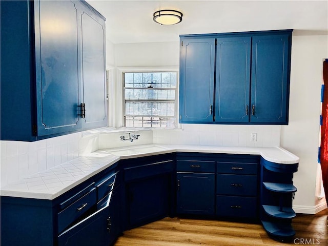 155 E Century Blvd, Los Angeles, CA 90003 - kitchen featuring blue cabinets, a sink, light countertops, light wood-type flooring, and tasteful backsplash