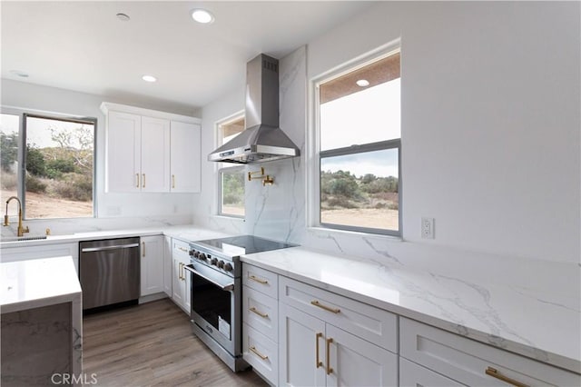 kitchen featuring a sink, recessed lighting, stainless steel appliances, white cabinets, and wall chimney range hood