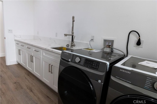 clothes washing area with a sink, wood finished floors, cabinet space, and washing machine and clothes dryer