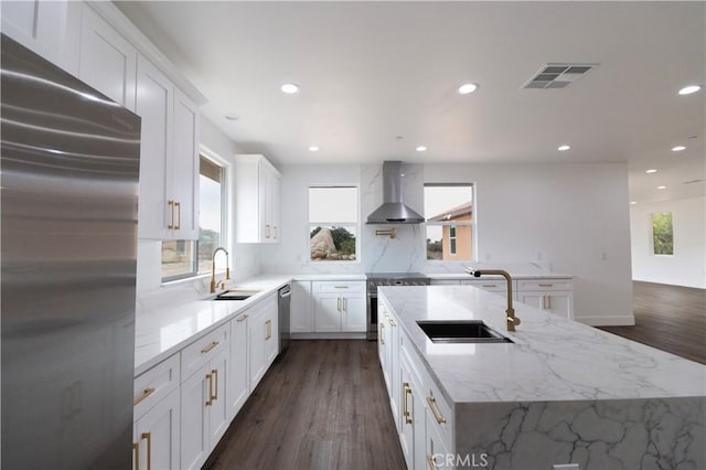 kitchen with a sink, stainless steel appliances, visible vents, and wall chimney range hood