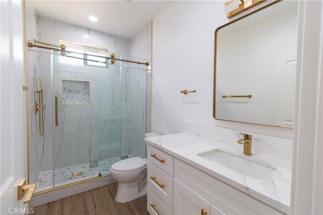 bathroom with a marble finish shower, toilet, wood finished floors, and vanity