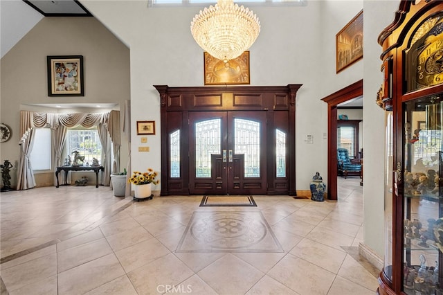 foyer with a towering ceiling, light tile patterned flooring, a notable chandelier, and baseboards