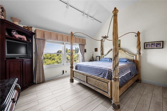 bedroom featuring track lighting, baseboards, light wood-style floors, and vaulted ceiling