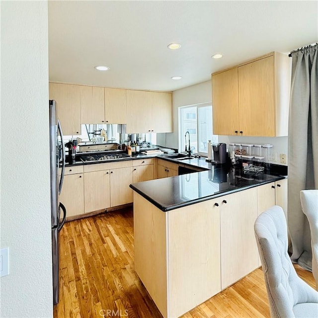 kitchen with light brown cabinets, light wood finished floors, a peninsula, a sink, and stainless steel appliances