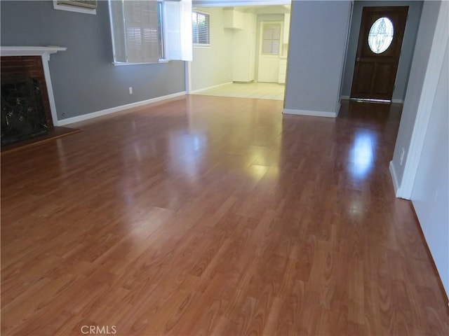 unfurnished living room featuring a brick fireplace, baseboards, and wood finished floors