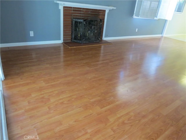 unfurnished living room featuring baseboards, a brick fireplace, and wood finished floors
