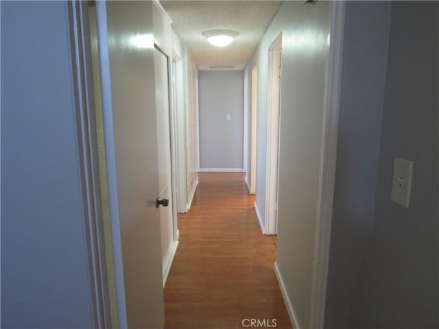 corridor with a textured ceiling, baseboards, and wood finished floors