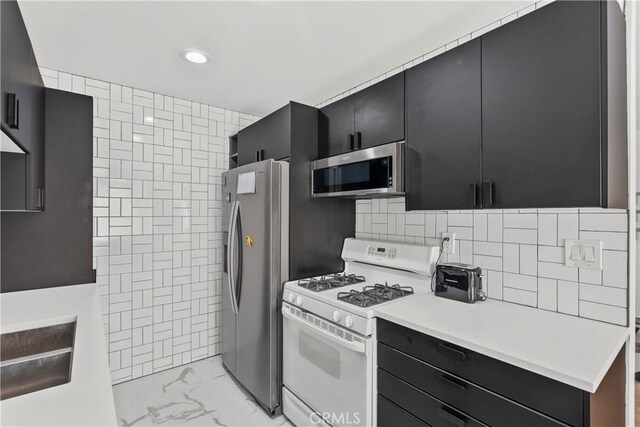 kitchen with light countertops, dark cabinetry, appliances with stainless steel finishes, marble finish floor, and tile walls