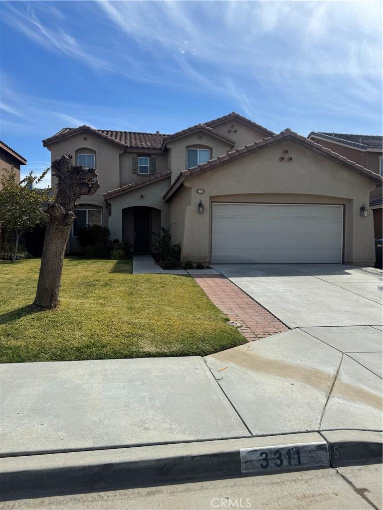 mediterranean / spanish home featuring a front lawn, a tile roof, concrete driveway, stucco siding, and a garage