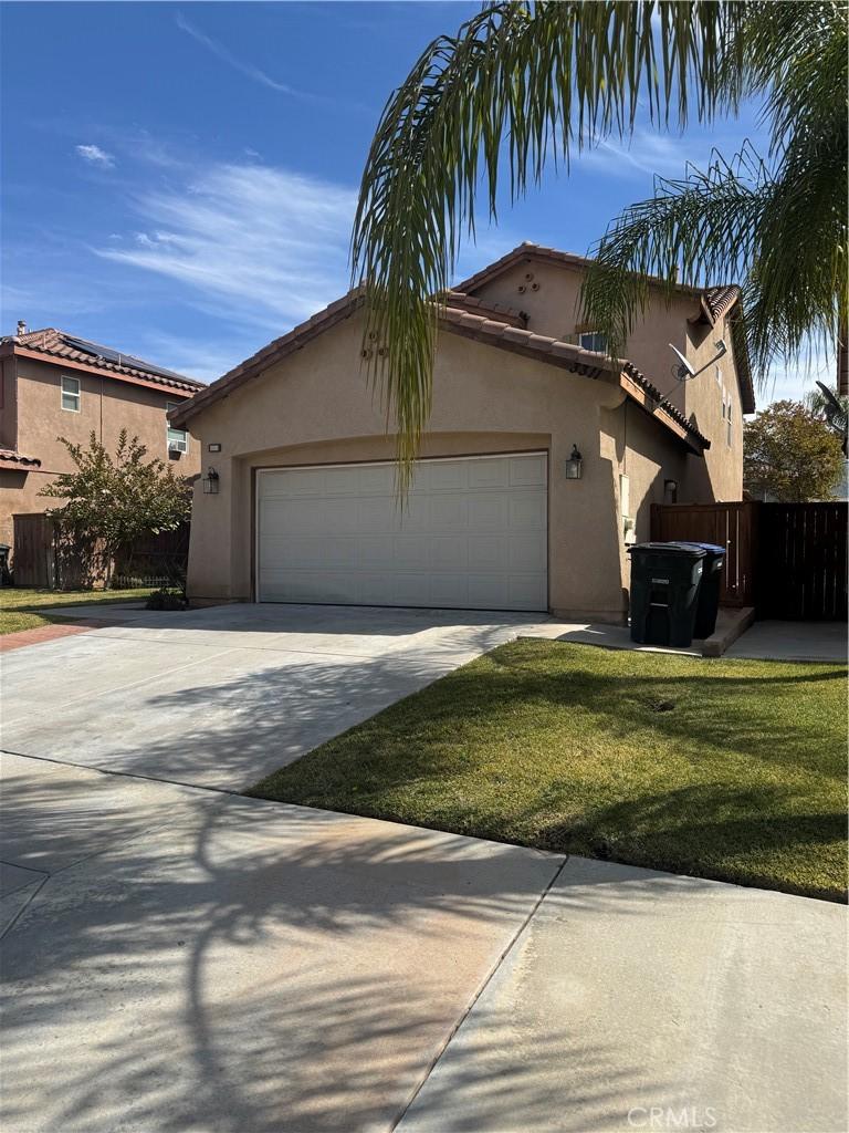 view of front of house featuring fence, driveway, an attached garage, stucco siding, and a front lawn