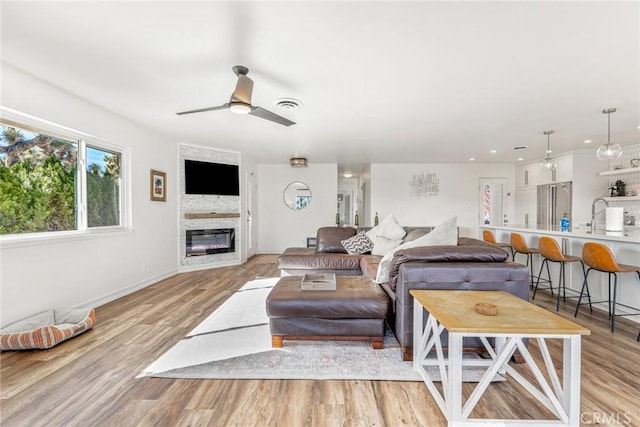 living room featuring a ceiling fan, baseboards, a glass covered fireplace, and light wood-style flooring