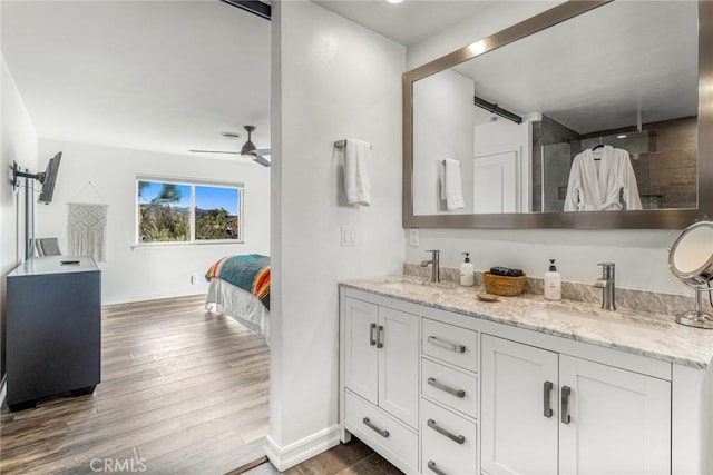 ensuite bathroom with baseboards, double vanity, a sink, and wood finished floors