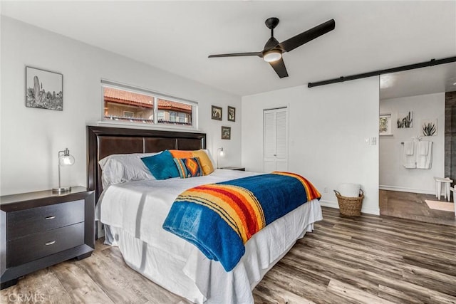 bedroom featuring wood finished floors, a closet, a barn door, baseboards, and ceiling fan