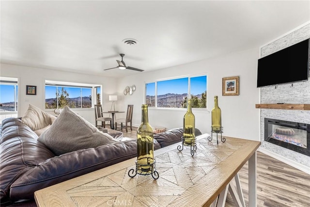 living room with ceiling fan, a stone fireplace, plenty of natural light, and wood finished floors