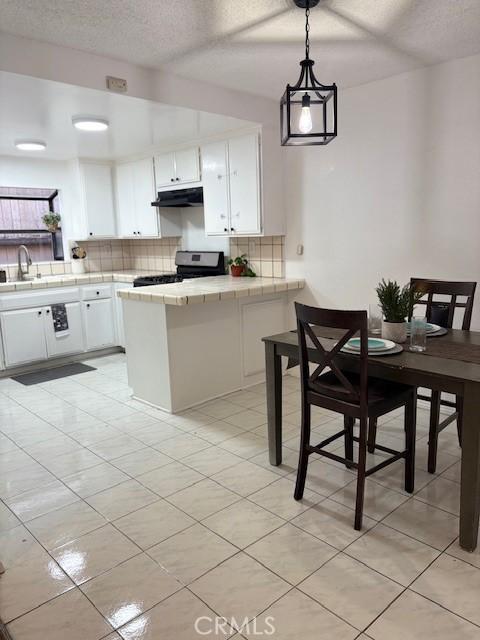 kitchen with a sink, stainless steel range with gas stovetop, decorative backsplash, under cabinet range hood, and white cabinetry