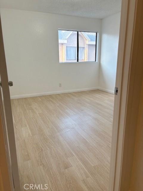 unfurnished room featuring light wood finished floors, a textured ceiling, and baseboards