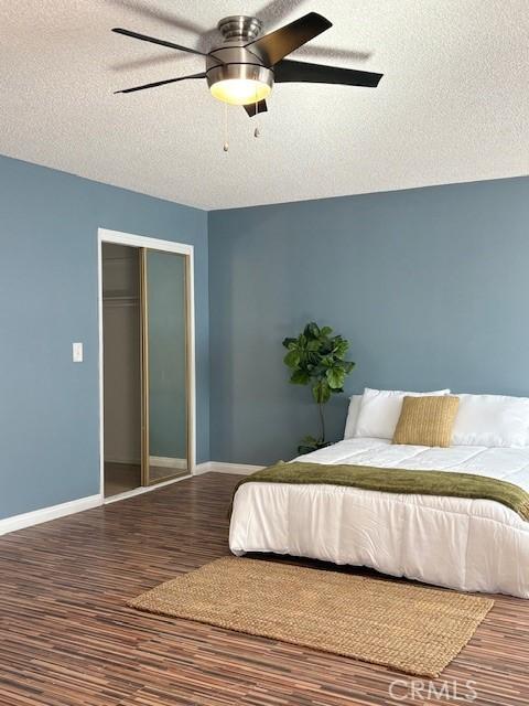 bedroom featuring wood finished floors, a closet, baseboards, a ceiling fan, and a textured ceiling