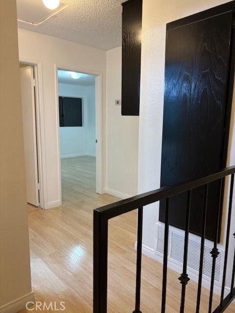 corridor with baseboards, light wood-type flooring, an upstairs landing, and a textured ceiling