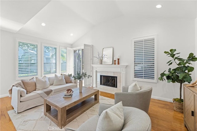 living room featuring lofted ceiling, a tile fireplace, baseboards, and light wood-style flooring