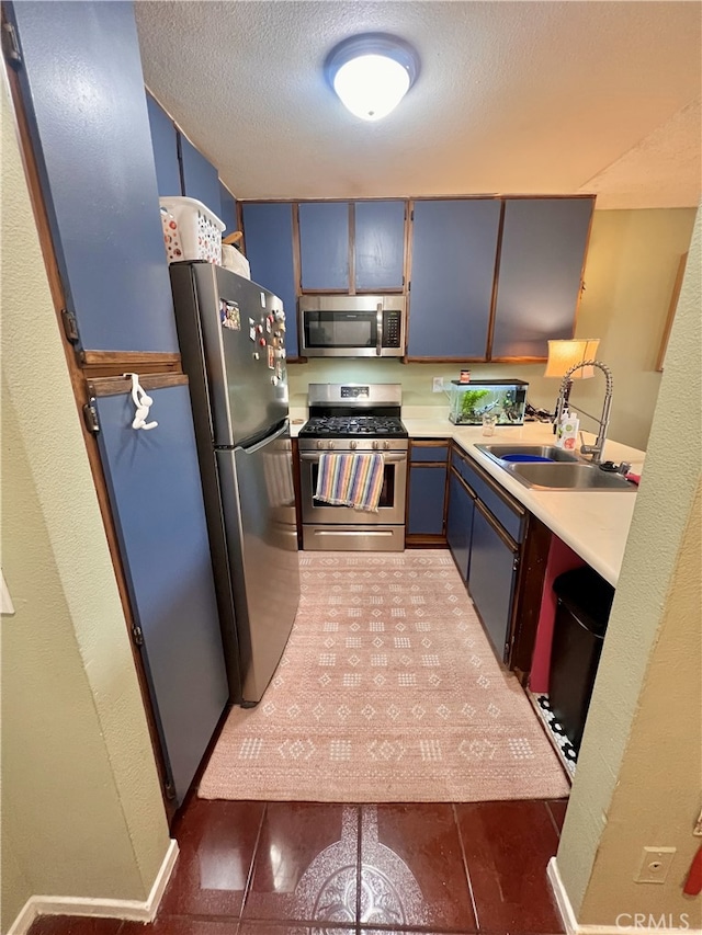 kitchen with stainless steel appliances, light countertops, blue cabinets, a sink, and a textured ceiling