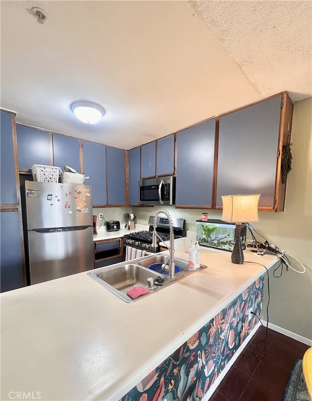 kitchen with a textured ceiling, light countertops, blue cabinetry, baseboards, and appliances with stainless steel finishes