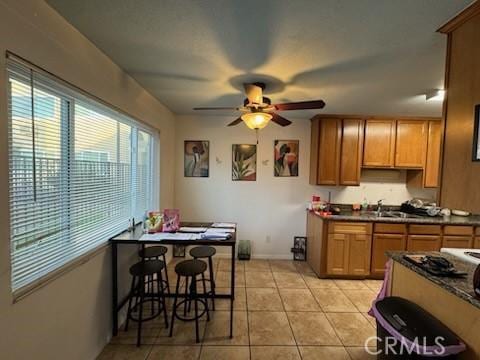 505 E Madison Ave Unit 84, El Cajon, CA 92020 - kitchen featuring light tile patterned floors, baseboards, ceiling fan, dark countertops, and brown cabinets