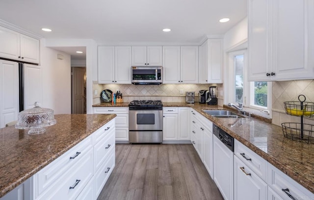 kitchen featuring stainless steel appliances, a sink, white cabinetry, light wood-style floors, and decorative backsplash