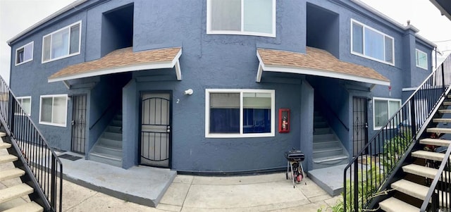view of front of home featuring stairway, stucco siding, and a shingled roof