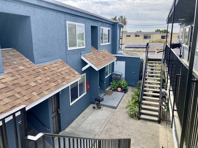 exterior space with a patio area, stucco siding, stairs, and roof with shingles