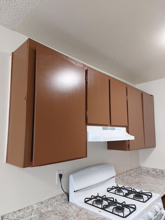 interior details with white range with gas cooktop, light countertops, under cabinet range hood, and a textured ceiling