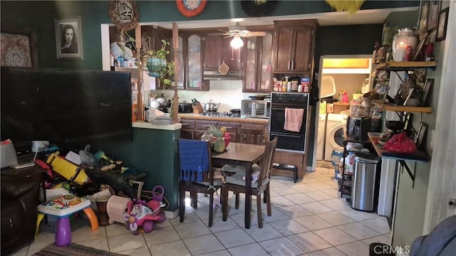 kitchen with light tile patterned flooring, stainless steel gas cooktop, black oven, a ceiling fan, and washer / dryer