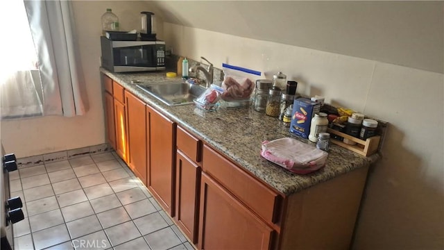 kitchen featuring a sink, stainless steel microwave, light tile patterned floors, and brown cabinets